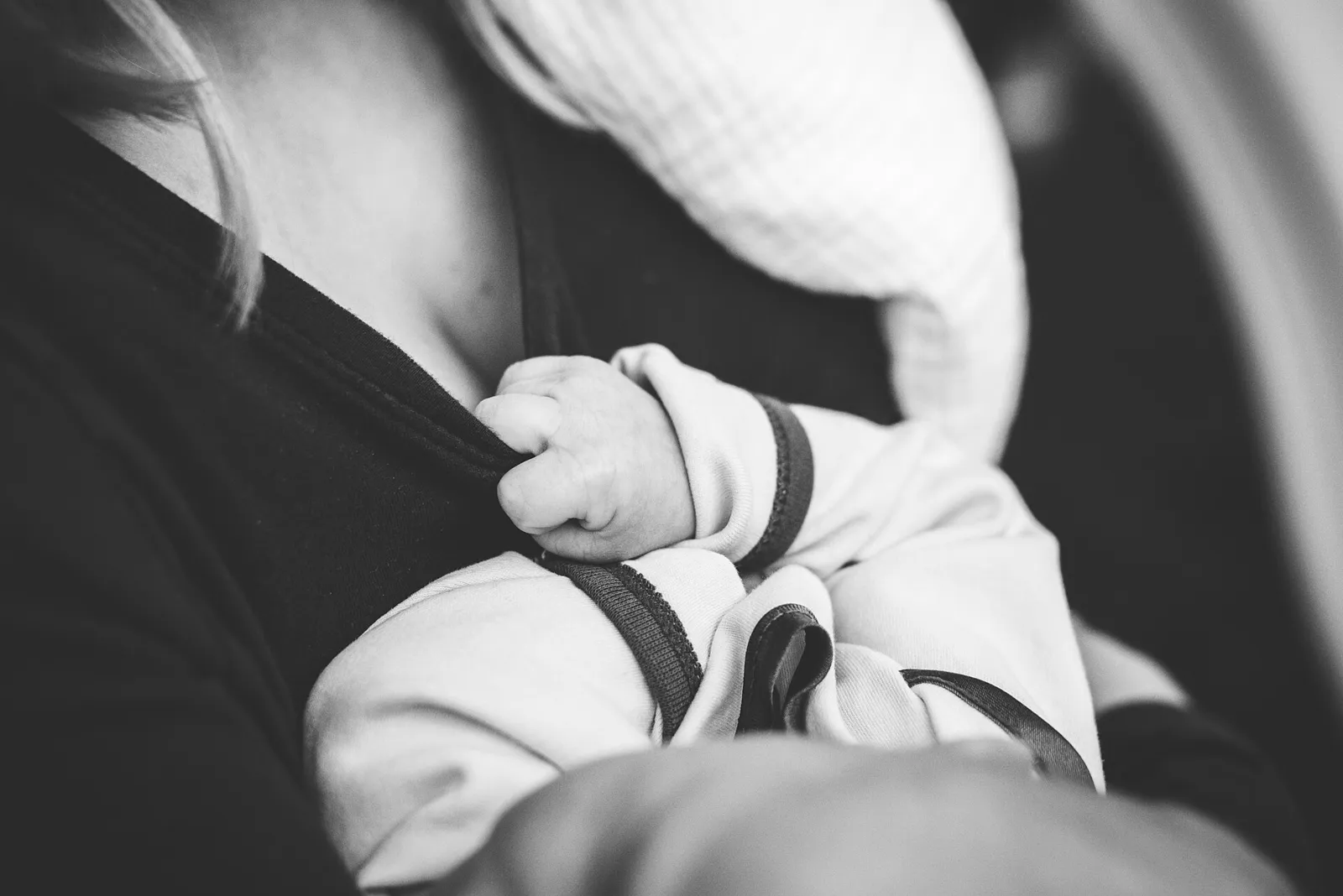 어른 품에 안긴 아기가 옷깃을 꼭 잡고 있는 흑백 사진, 아기 얼굴은 보이지 않음